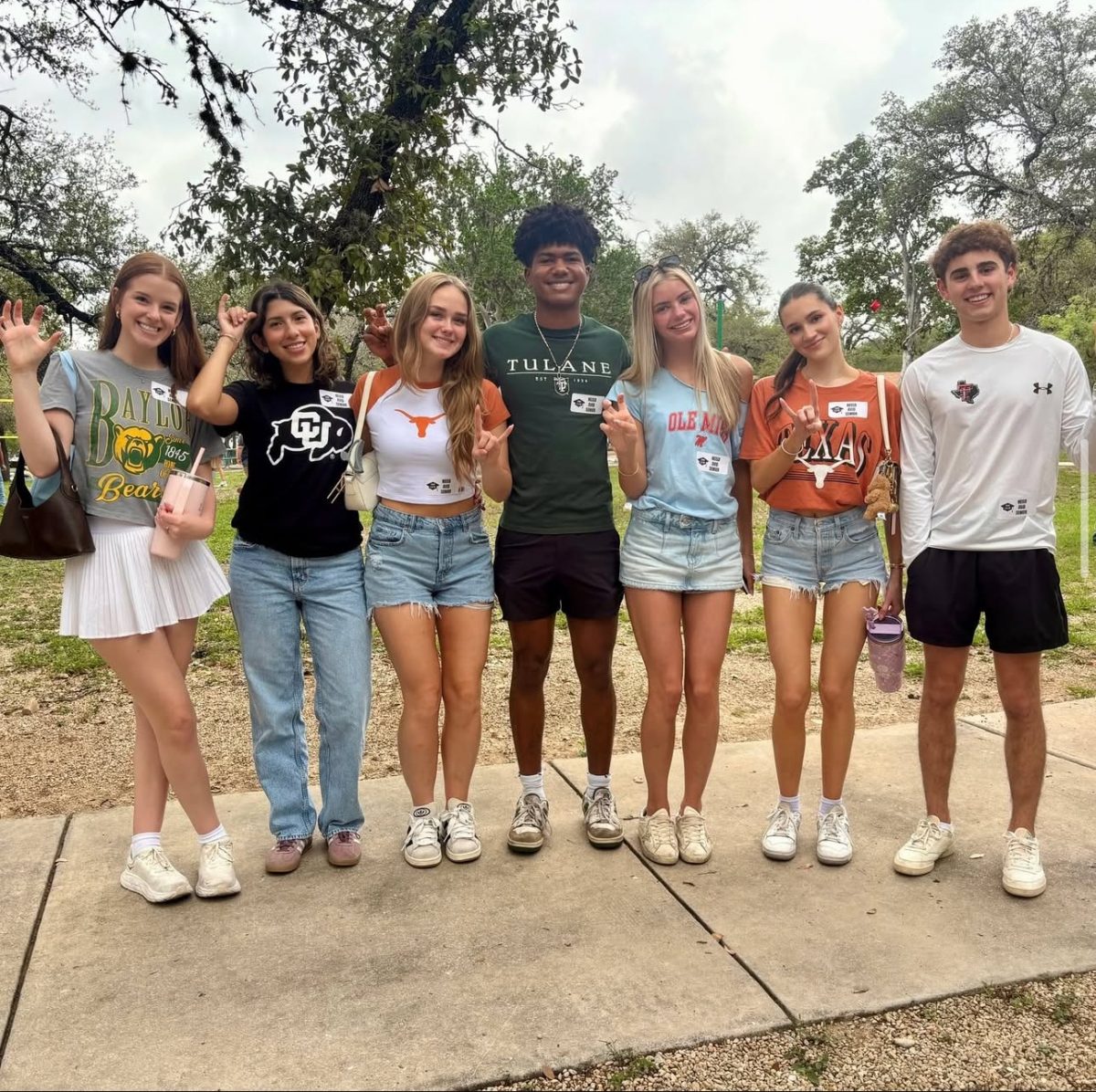 Going from left to right: Lourdes Redmond, Sophia Gutierrez, Harper Hutchison, Valmor Delameda, Grace Flath, Paisley Sharpe, and Vincent Bates all wear college t - shirts of the colleges they've committed to.